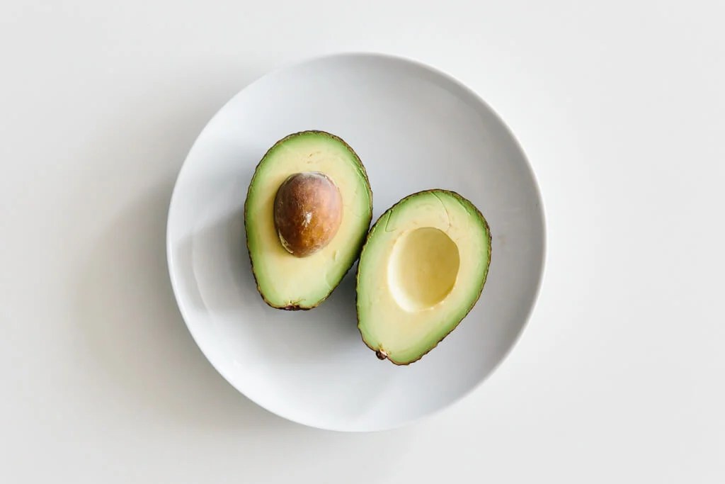 Plate of avocado sliced in half on a white table.