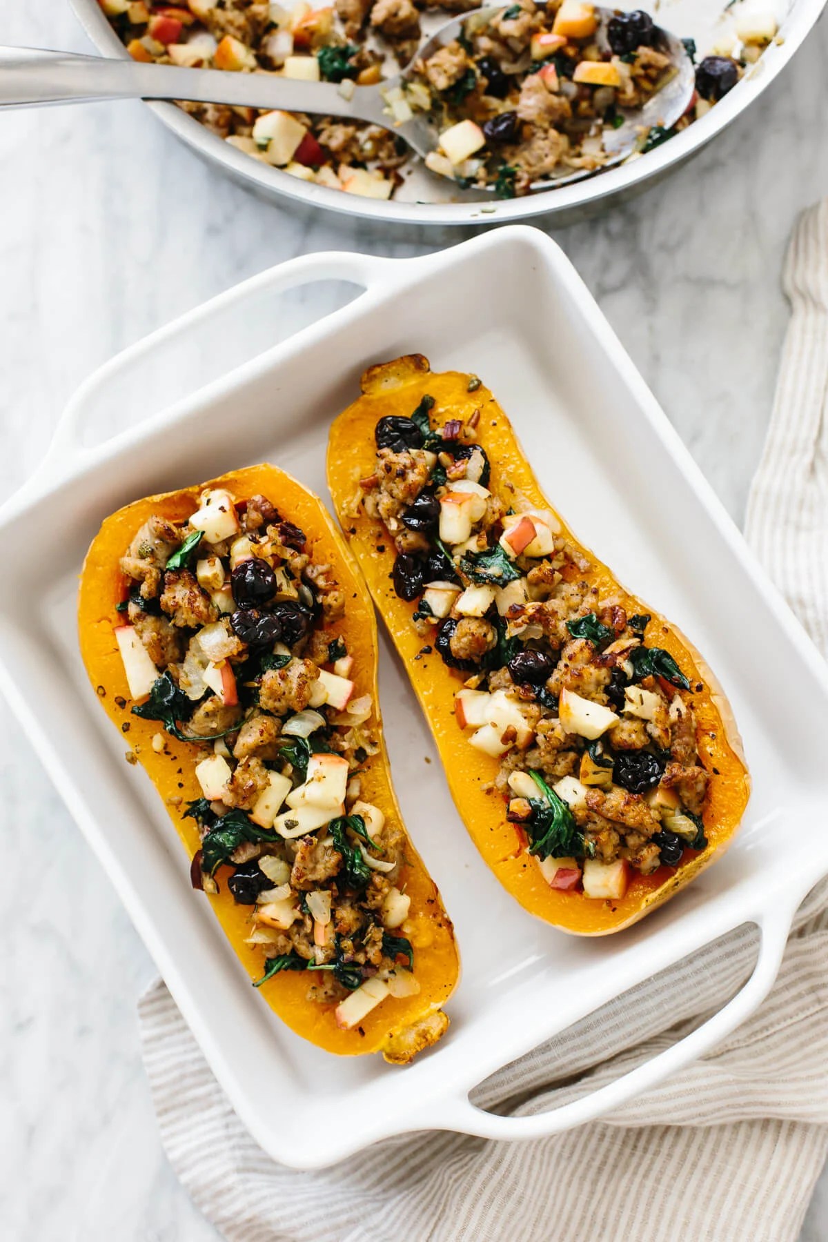 Butternut squash filled with sausage apples and other ingredients in a baking dish.