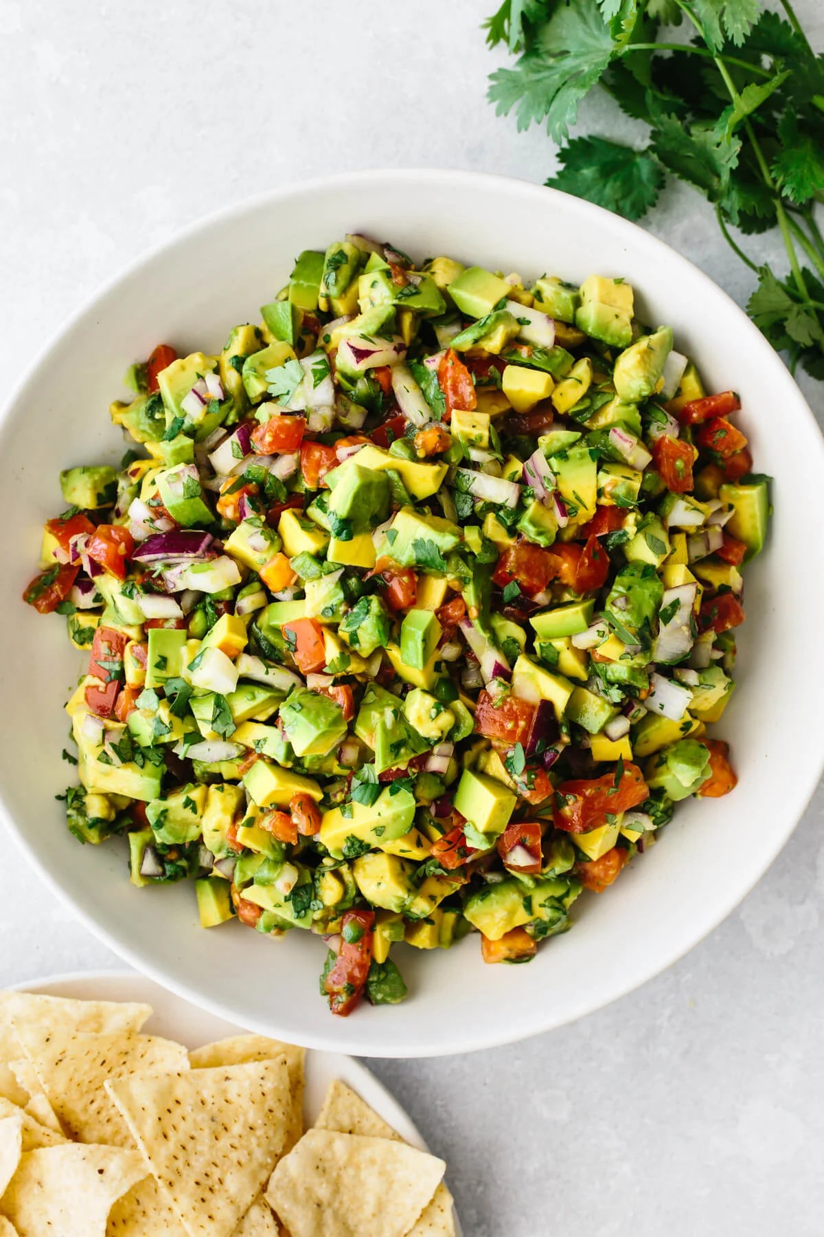 A big bowl of avocado salsa next to a plate of chips.