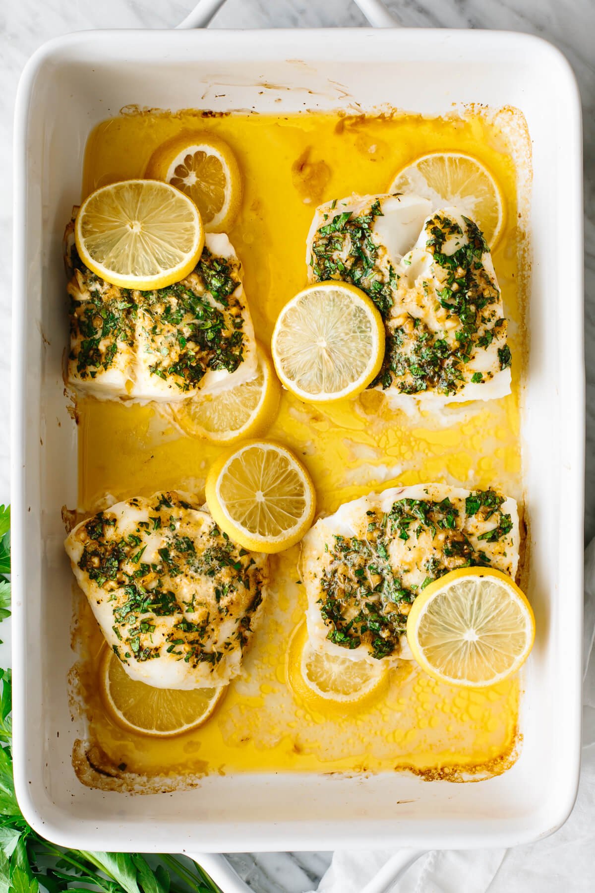 Baked cod with lemon slices in a baking dish.
