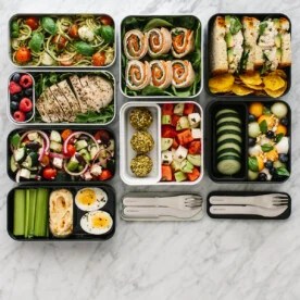 Several bento boxes on a table with different lunch recipes and ingredients.