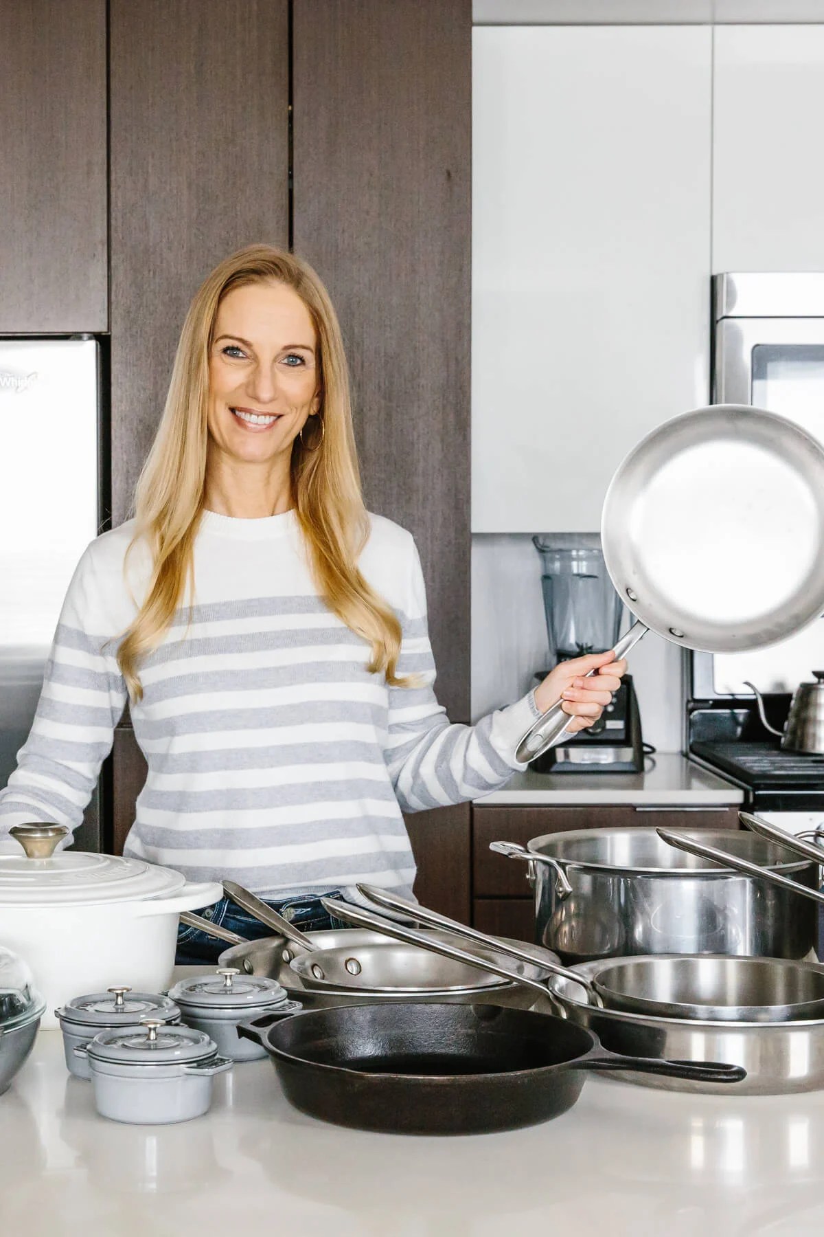 The best cookware types all on a counter with girl holding stainless steel pan.