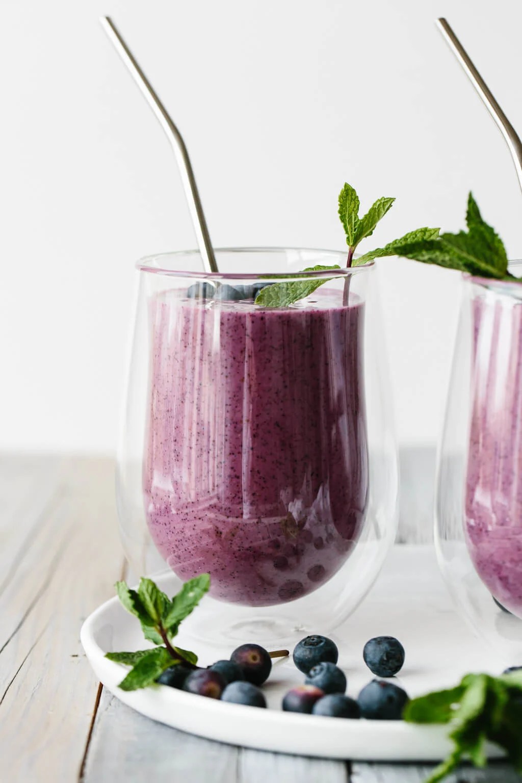 Blueberry smoothie in a glass with straw.