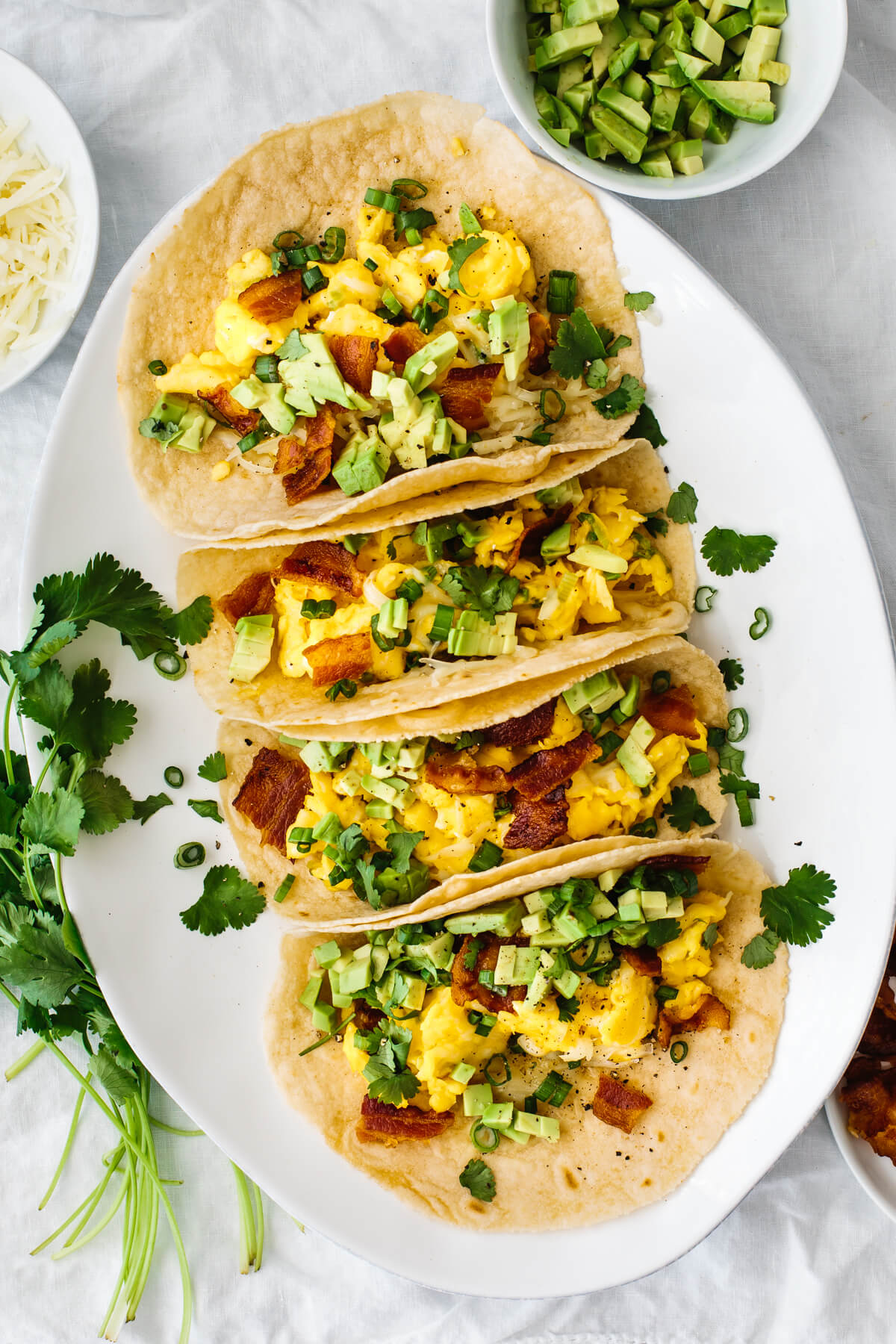 Breakfast tacos on a plate next to cilantro and avocado.