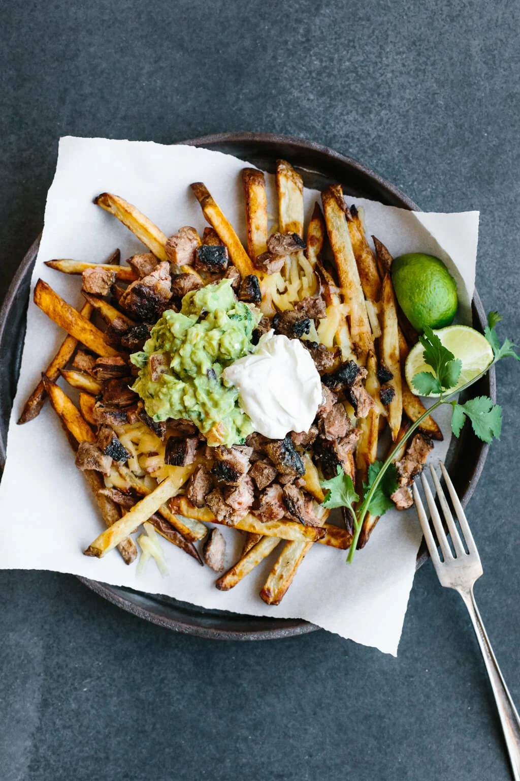 Fries topped with carne asada, guacamole and sour cream on a plate.