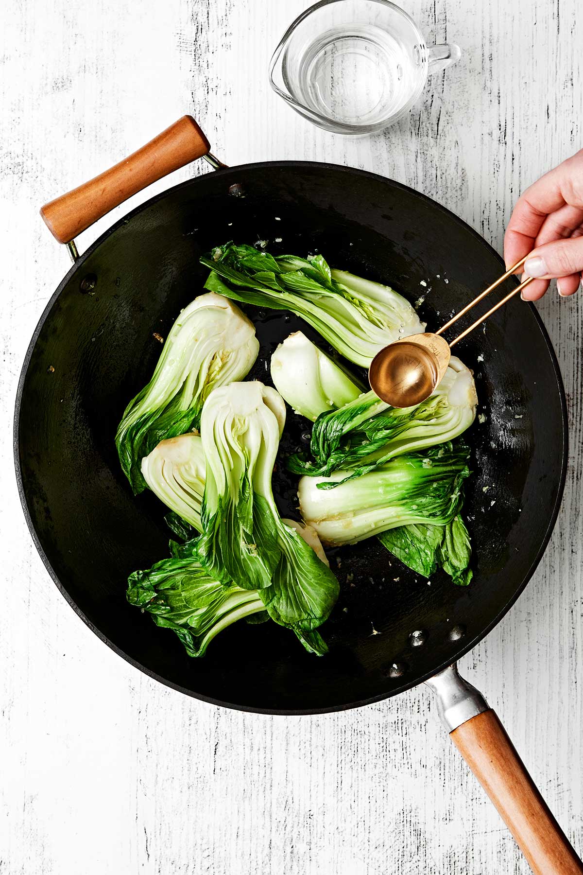 Adding water to bok choy in a wok.