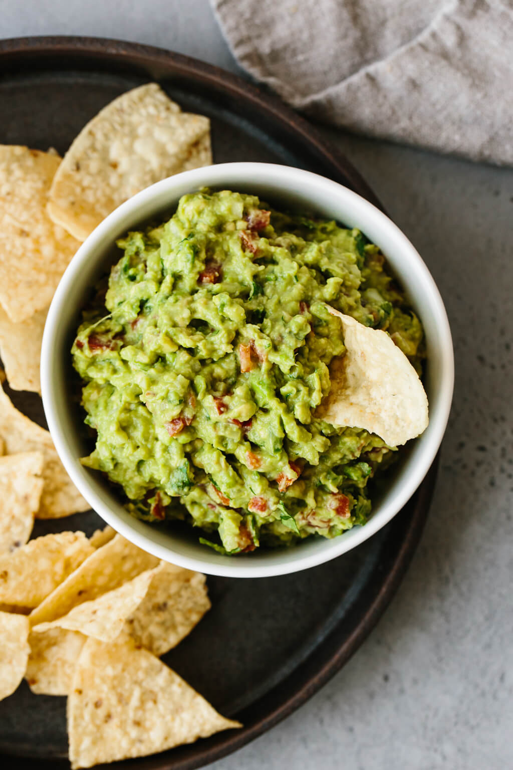 Guacamole in a bowl surrounded by chips. One chip in the guacamole.