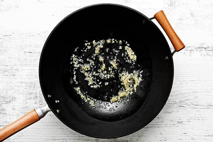 A wok with garlic, ginger, and oil.