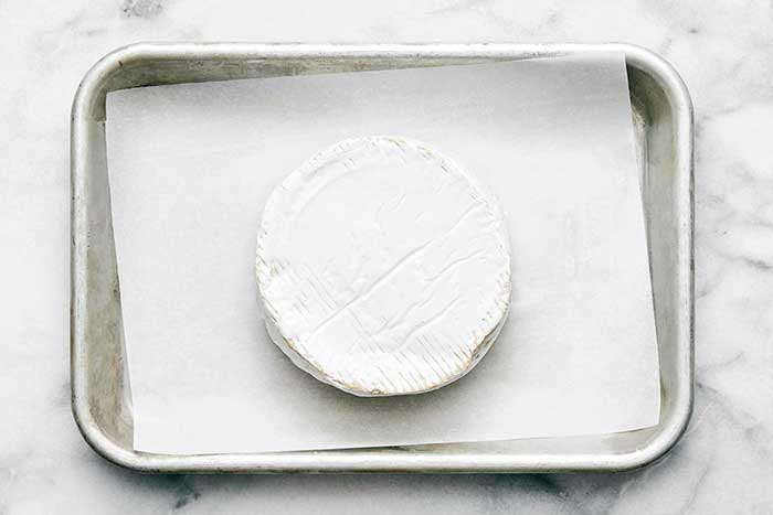 A sheet pan with parchment paper and brie.