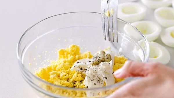 Mixing the deviled egg filling ingredients in a bowl.