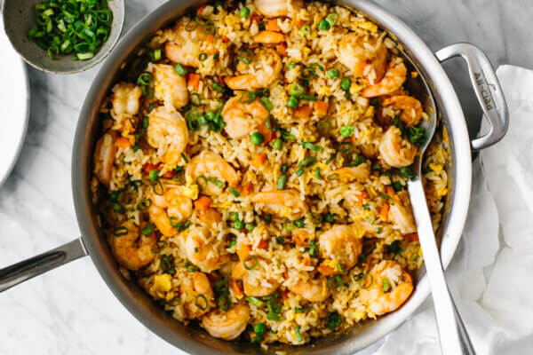 A large pan of shrimp fried rice next to green onions.