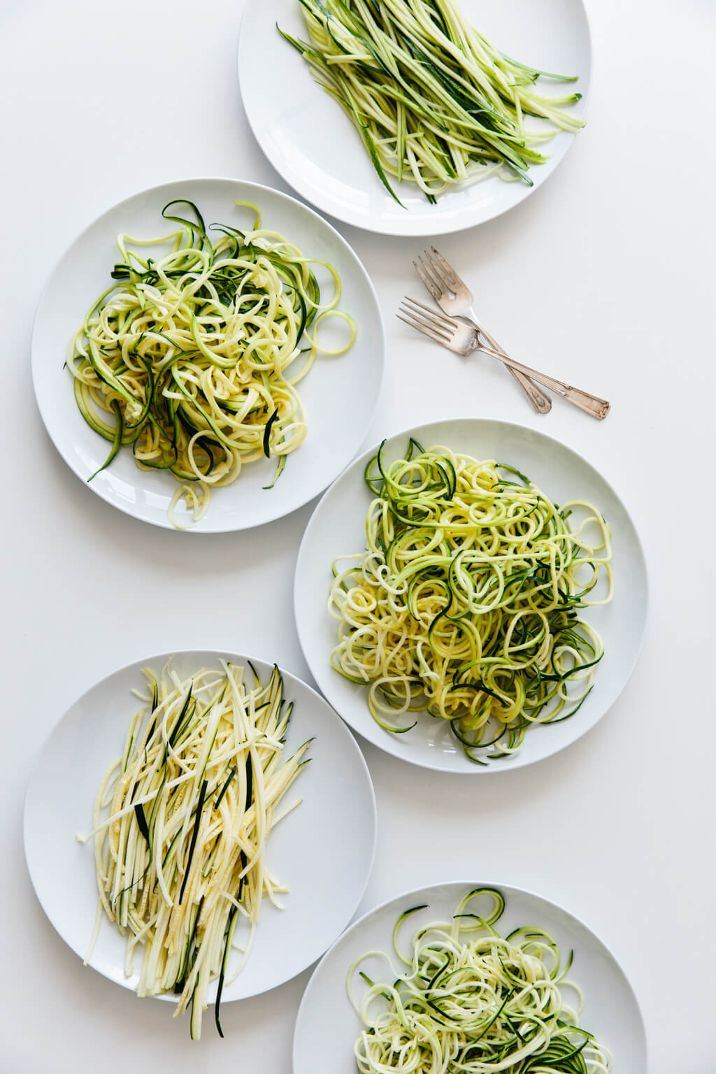 Five plates of zucchini noodles made by different methods.