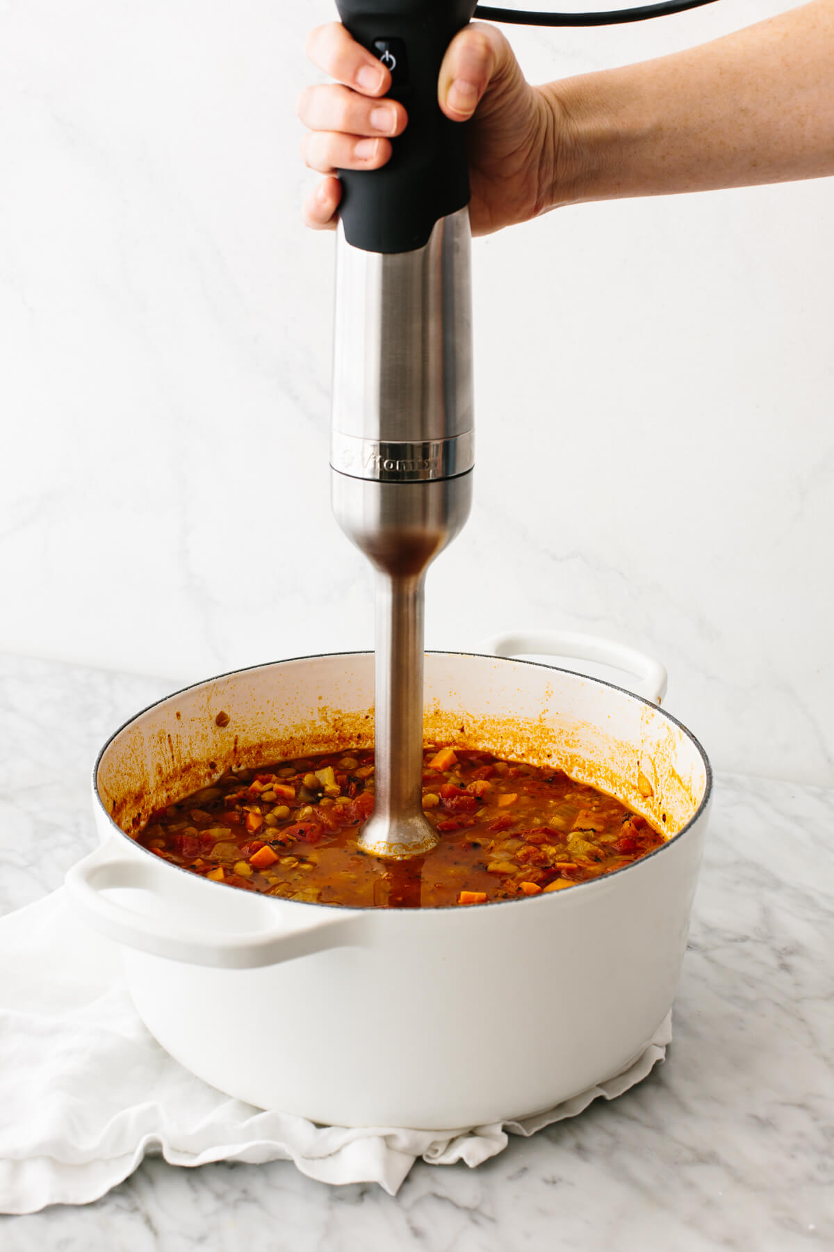 Using an immersion blender to spot blend a lentil soup in a pot.
