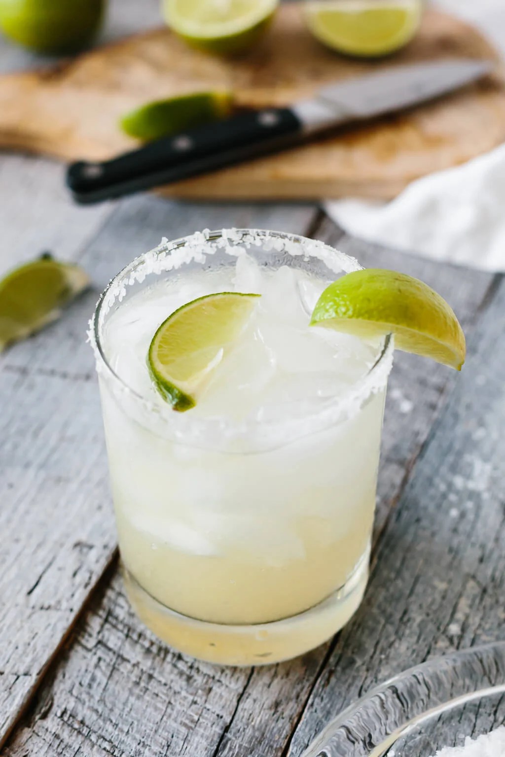 Margarita in a glass with limes on top and in the background.