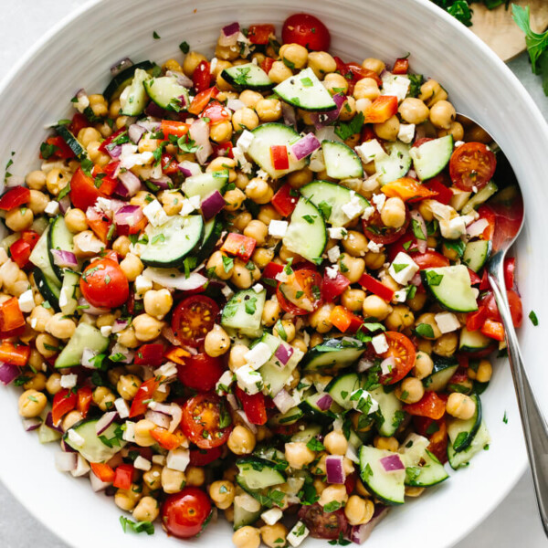 A large white bowl of Mediterranean chickpea salad on a table with parsley leaves.