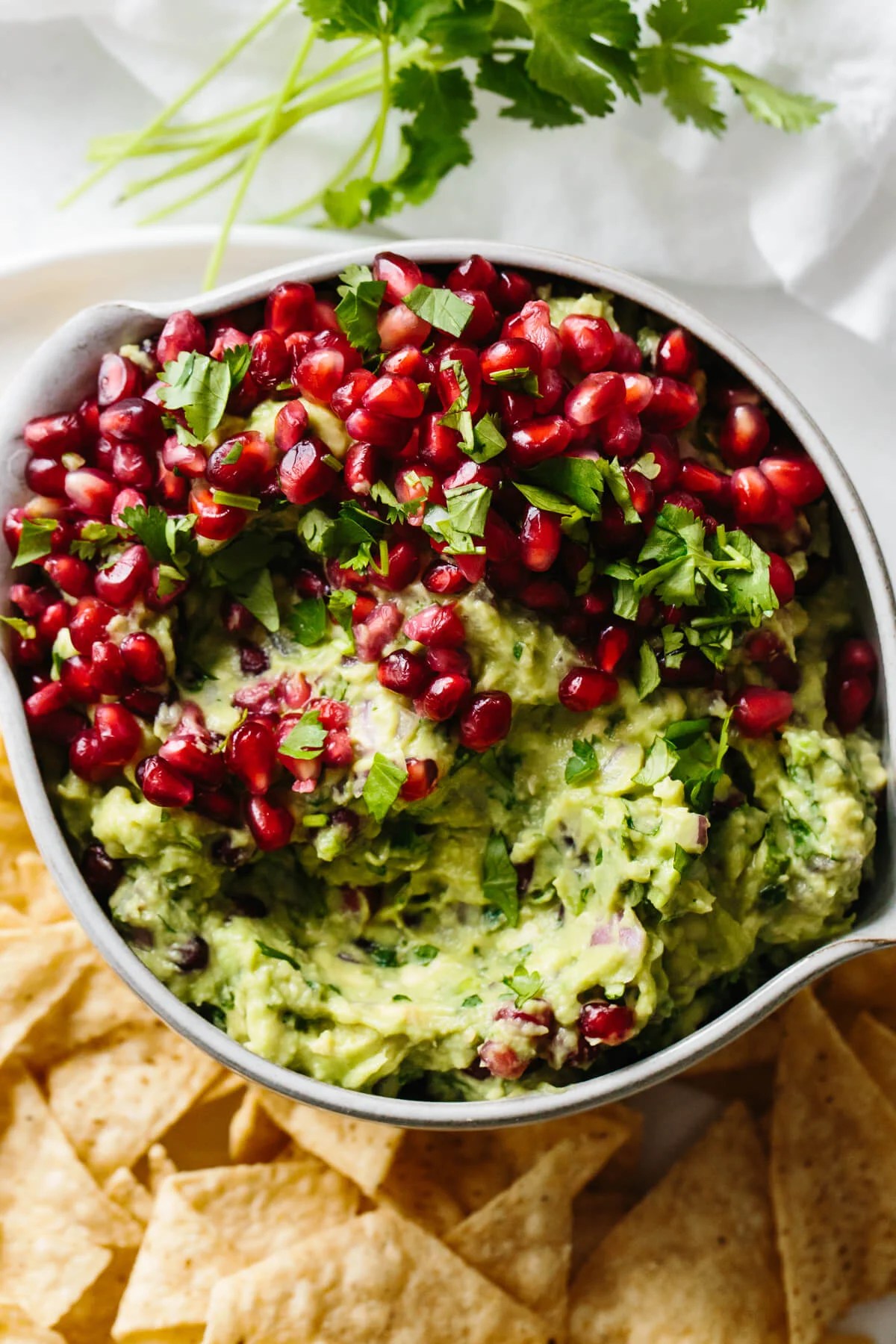 Pomegranate guacamole in a bowl surrounded with tortilla chips.