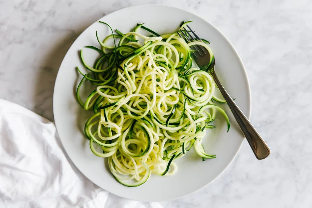 Raw zucchini noodles on a plate with fork.