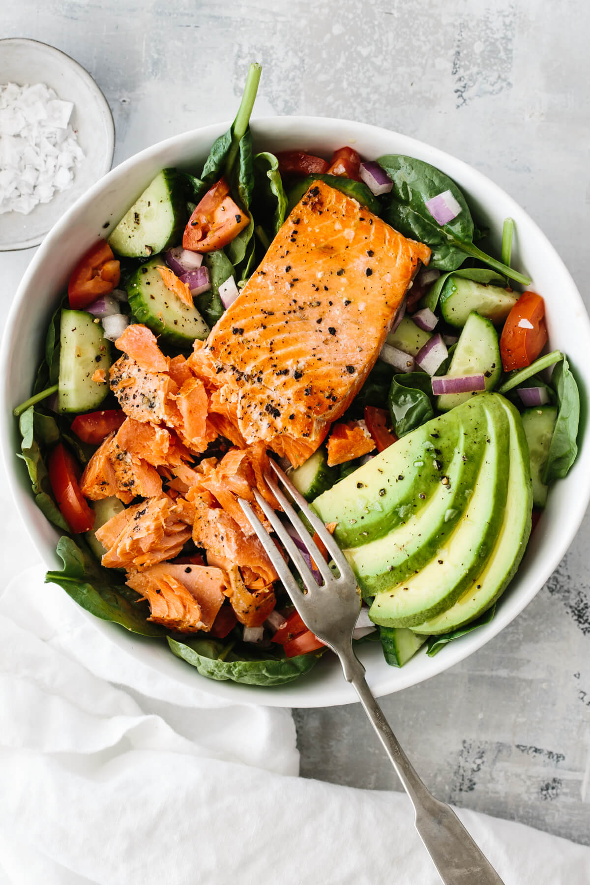 Salmon fillet on salad with avocado slices.