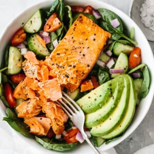 Salmon filet broken up with fork on top of salad with avocado slices.