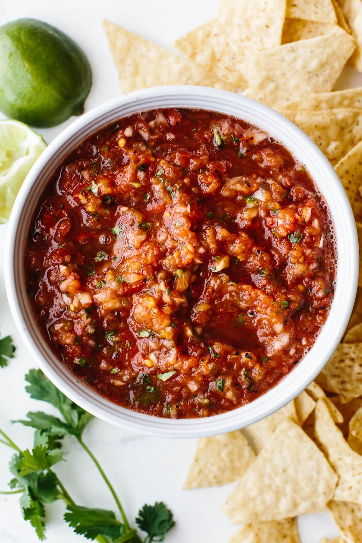 Salsa recipe in a bowl surrounded by chips, limes and cilantro.