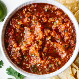 Salsa recipe in a bowl next to chips, lime slices and cilantro.