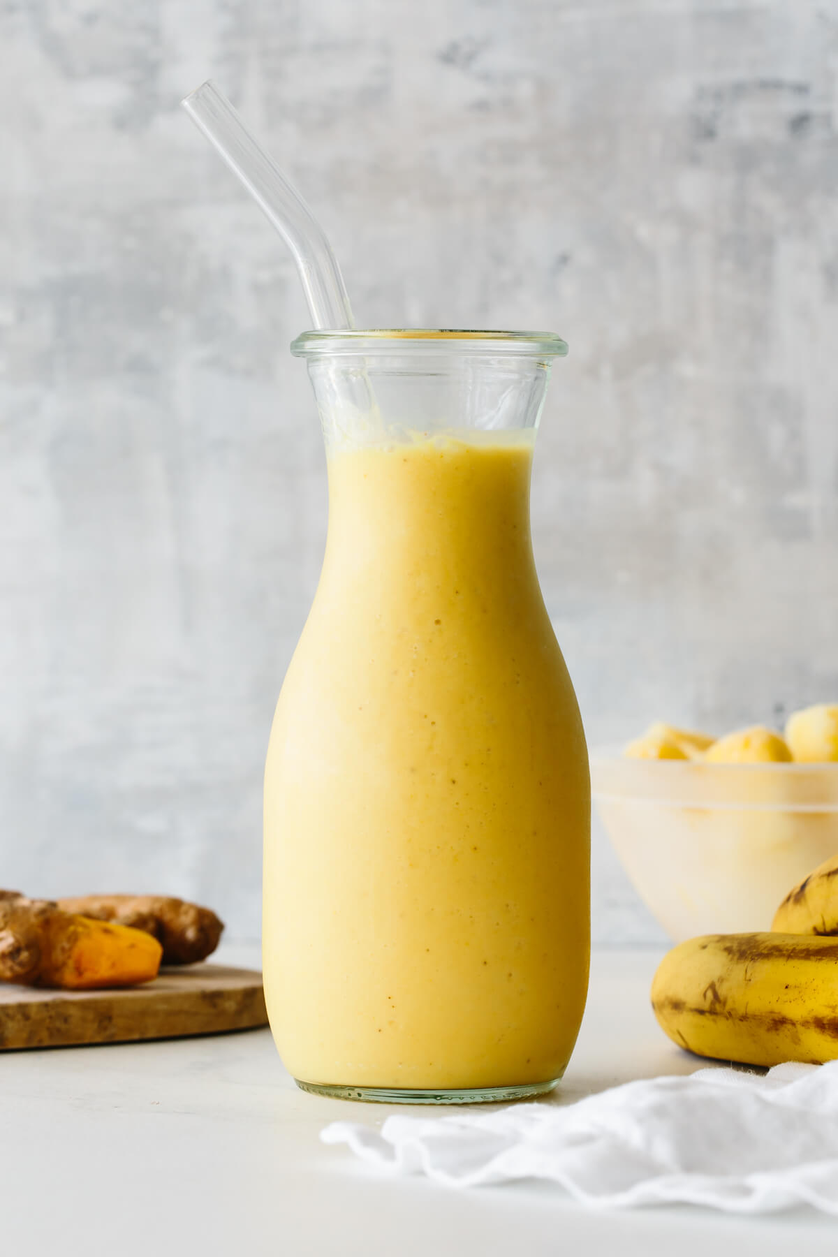 Turmeric smoothie in a glass jar with straw and ingredients in the background.