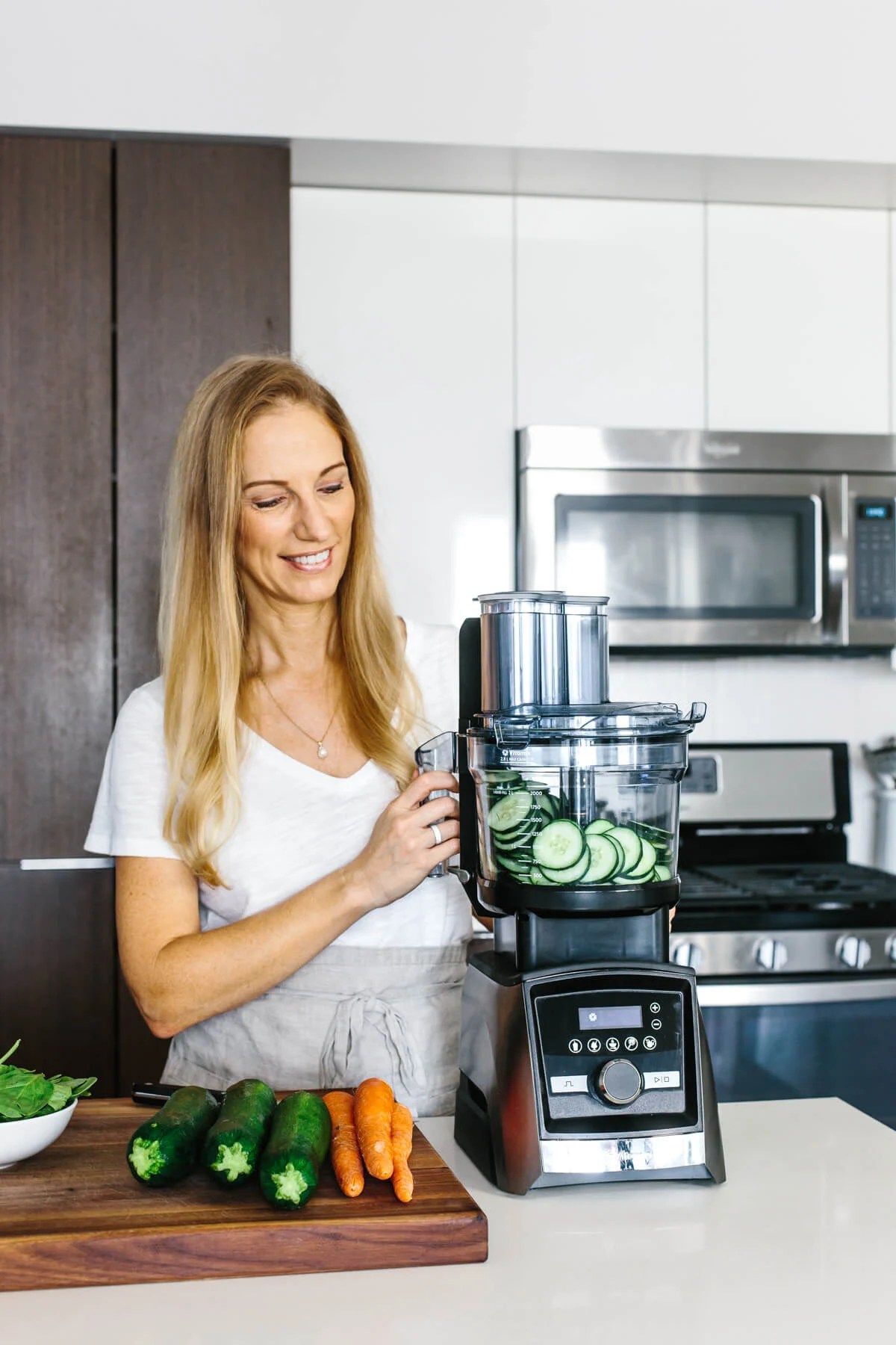 Girl looking at Vitamix food processor with sliced cucumber inside.