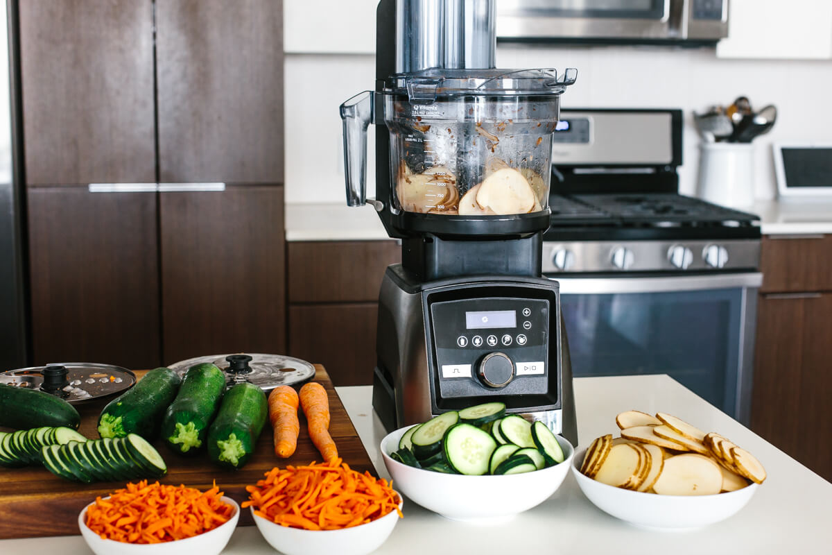 Bowls of sliced and shredded vegetables in front of the Vitamix food processor.